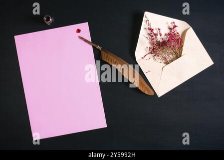 Enveloppe ouverte pleine de fleurs rouges, un stylo à plume antique sur une note de papier rose avec une éclaboussure d'encre rouge sur un fond en bois noir Banque D'Images