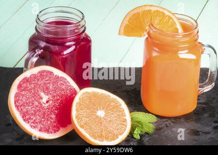 Jus d'orange fraîchement pressé et nectar de pamplemousse, dans des pots mason, sur un plateau de pierre noire, avec des tranches d'orange et de pamplemousse et des feuilles de menthe à proximité Banque D'Images