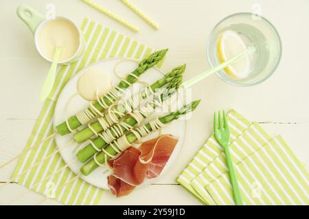 Asperges vertes cuites à la vapeur sur des brochettes en bois avec des spaghettis enveloppés de sauce hollandaise et de jambon Banque D'Images