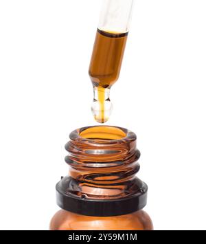 Goutte à goutte de l'huile d'une pipette dans une bouteille en verre close-up isolé sur fond blanc Banque D'Images