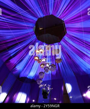 Regardant une tente de cirque bleue et violette, avec des projecteurs pointés sur des chapeaux dorés et argentés suspendus sur l'étalage et un chapeau noir rempli Banque D'Images