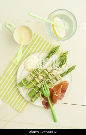 Asperges vertes cuites à la vapeur sur des brochettes en bois avec des spaghettis enveloppés de sauce hollandaise et de jambon Banque D'Images