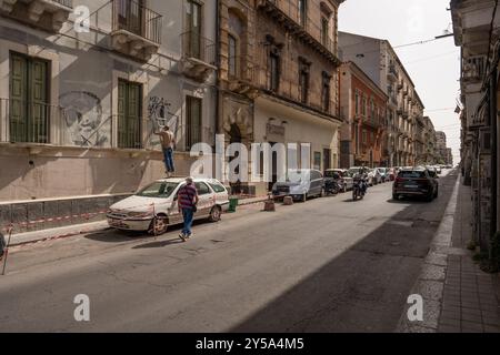 Catane, Italie - 20 mai 2024 : scène de rue à Catane avec un homme sur une échelle enlevant graffiti du mur. Banque D'Images