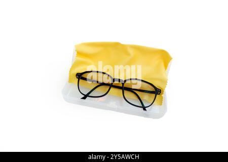 une paire de lunettes à bordure noire, reposant sur un chiffon en microfibre jaune, soigneusement niché dans un boîtier en plastique transparent. Banque D'Images