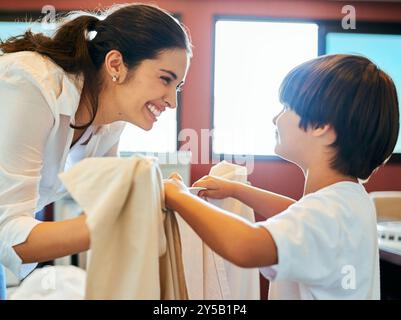 Blanchisserie, maman et fils travaillant ensemble avec les soins, les liens heureux et le développement de l'enfant à la maison. Ménage, mère et enfant pliant des vêtements pour l'aide Banque D'Images