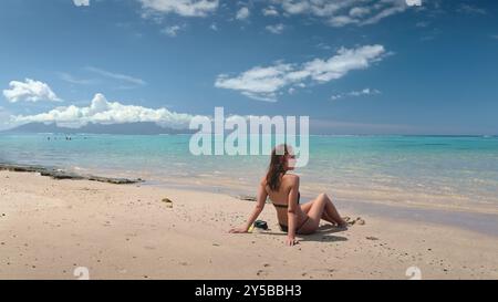 Jeune femme profite du soleil chaud et de la douce brise alors qu'elle se détend sur une plage de sable immaculée, son équipement de plongée avec tuba reposant à côté d'elle Banque D'Images