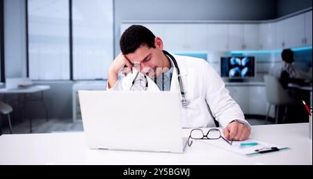 Fatigué jeune médecin masculin se reposant à Computer Desk à l'hôpital Banque D'Images