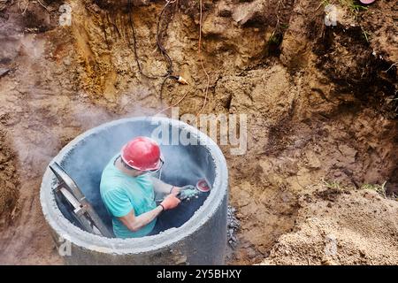 Utilisation d'une meuleuse d'angle lors de la construction de fosse septique à partir d'anneaux en béton. Banque D'Images