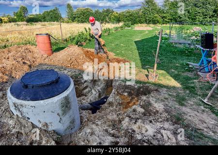 Une tranchée d'absorption avec tuyau de drainage perforé enveloppé dans du géotextile est remplie de terre à l'aide d'une pelle à baïonnette. Banque D'Images