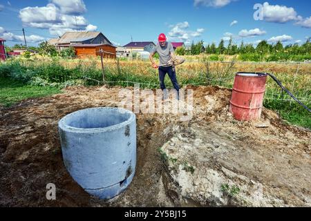 Constructeur enterre des anneaux de fosse septique en béton pendant l'installation du système d'égout pour la maison de campagne. Banque D'Images