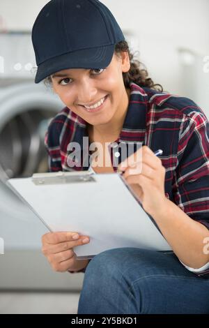 heureuse jeune femme technicien écrivant sur presse-papiers dans la cuisine Banque D'Images