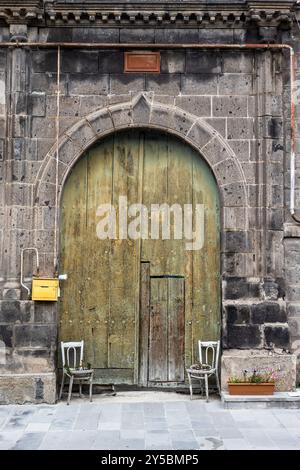 Porte en bois avec guichet dans la vieille maison faite de tuf noir sur la rue dans la ville de Gyumri, Armrnia le jour d'été couvert Banque D'Images