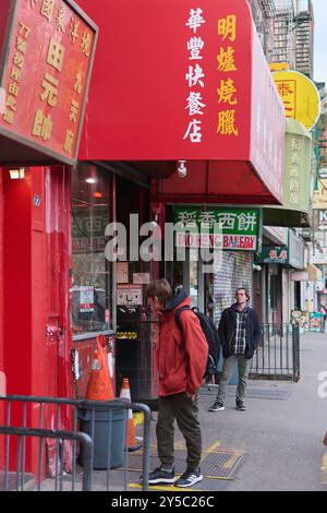 New York, États-Unis - 21 septembre 2024 : image d'une rue animée de Chinatown avec la façade rouge de TAO HONG Bakery et des panneaux en chara chinois Banque D'Images