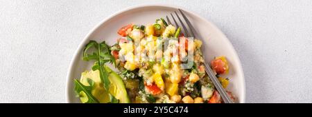 Une salade végétarienne vibrante composée de millet bouilli, de pois chiches, de légumes frais et d'avocat, arrosée d'huile d'olive pour un repas délicieux et sain Banque D'Images