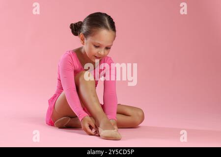 Petite ballerine mettant sur des chaussures pointe sur fond rose, espace pour le texte Banque D'Images