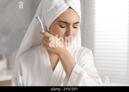 Jeune femme avec brosse à dents souffrant de maux de dents dans la salle de bain Banque D'Images