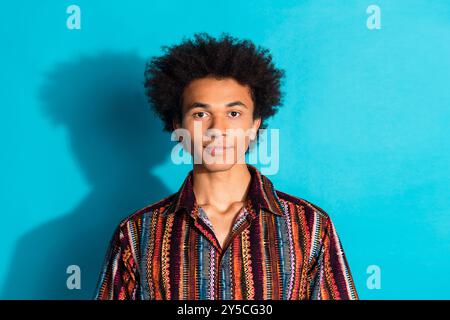 Portrait photo du jeune beau gars américain avec les cheveux ondulés portant chemise rayée d'été isolé sur fond de couleur cyan Banque D'Images