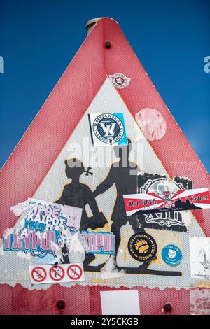 panneau d'avertissement triangulaire bordé de rouge pour les enfants qui traversent la route devant eux couverts d'autocollants par des vandales. Banque D'Images