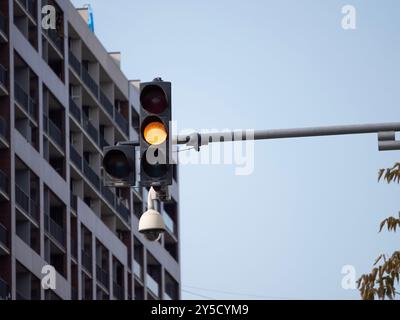 Un feu de circulation avec un feu jaune est sur une rue devant un bâtiment. Une caméra de sécurité CCTV est montée sur le feu tricolore. Photo de haute qualité Banque D'Images