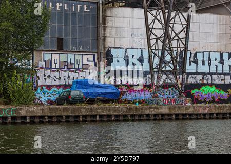 Maastricht, Limbourg du Sud, pays-Bas. 30 août 2024. Rue mal entretenue avec des ordures par la rivière, mur couvert de graffitis d'une ancienne usine, parke Banque D'Images