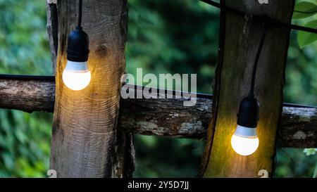 Petites ampoules décorées le long d'une clôture en bois rustique dans un restaurant local, projetant une lueur chaleureuse et confortable. L'éclairage doux améliore l'atmo invitant Banque D'Images