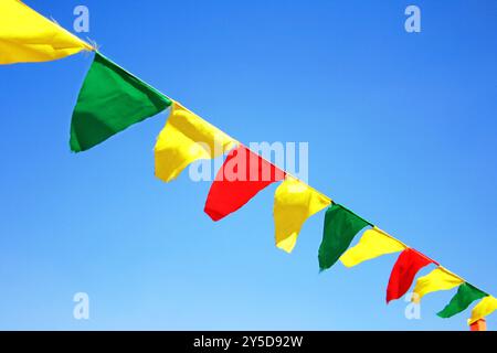 Ruban festif de drapeaux triangulaires multicolores sur les nuages blancs et fond de ciel bleu. Fête de célébration, foire de vacances, décorations de festival. Élevé Banque D'Images