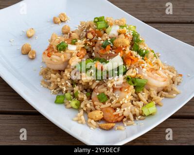 Un riz frit aux crevettes éclatant garni d'arachides croquantes, d'oignons verts frais et de graines de sésame grillées, magnifiquement exposé sur une assiette blanche contre Banque D'Images