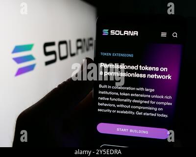 Dans cette illustration photo, une personne tient un téléphone portable avec la page Web de la société de plateforme blockchain Solana devant le logo de l'entreprise. Banque D'Images