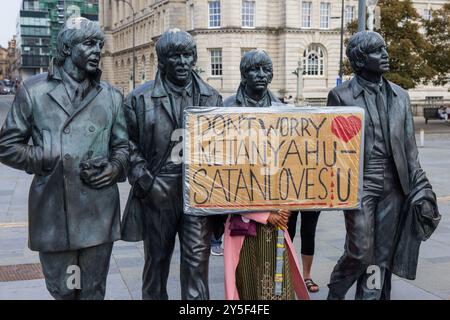 Liverpool, Royaume-Uni. 21 SEP, 2024. Le signe 'ne vous inquiétez pas netanyahu satan Loves u' est tenu à côté de la statue des beatles dans le cadre d'une marche nationale de Palestine, comme vu à Londres, des entraîneurs du Sud, Leeds et Manchester ont amené des activistes. Les militants se sont rassemblés à St George's Hall avant de marcher vers le quai près du port de Liverpool, cela arrive alors que la conférence du travail commence demain dans la ville. Crédit Milo Chandler/Alamy Live News Banque D'Images