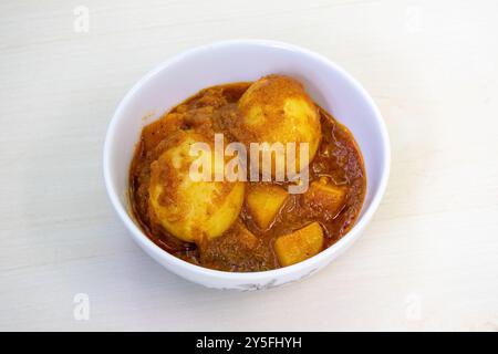 Curry aux œufs épicé ou Dim Vuna, cuit avec des pommes de terre, dans un bol en céramique blanche, placé sur une surface en bois clair. Le dim bhuna bouilli est un délicieux bengali Re Banque D'Images