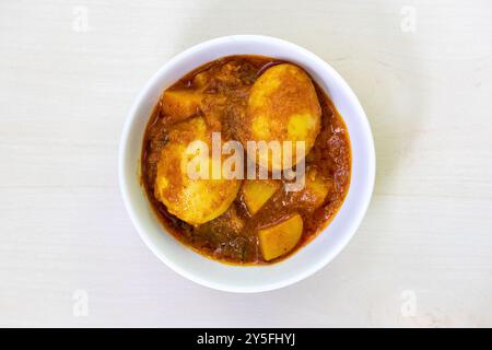 Curry aux œufs épicé ou Dim Vuna, cuit avec des pommes de terre, dans un bol en céramique blanche, placé sur une surface en bois clair. Vue de dessus de savoureux dim bhuna bouilli, a Banque D'Images