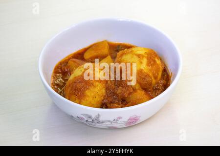 Curry aux œufs épicé ou Dim Vuna, cuit avec des pommes de terre, dans un bol en céramique blanche, placé sur une surface en bois clair. Le dim bhuna bouilli est un délicieux et tradit Banque D'Images