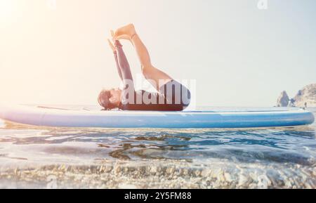 Yoga Paddleboard exercice Ocean Man pratiquer le yoga sur une planche à paddleboard dans l'océan au coucher du soleil Banque D'Images
