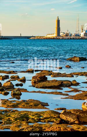 Le phare de Fanale dei Pisani vu de la côte rocheuse près de Terrazza Mascagni à Livourne, Italie, avec des marées reflétant le ciel. Banque D'Images