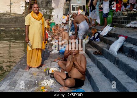 Un prêtre hindou (l) conduisant des rites pour les parents décédés d'hommes hindous, ces derniers ayant la tête rasée rituellement ; à Saint Banganga Tank, Mumbai, Ind Banque D'Images