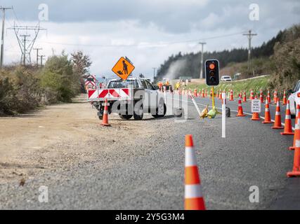 Panneau de signalisation routière sur le dessus du chariot de travail. Cônes orange sur la route. Les voitures s'arrêtèrent au feu rouge des travaux. Travailleurs méconnaissables sur la route. Banque D'Images