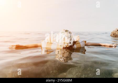 Femme Sea Float Relaxing - Une femme dans une robe blanche flotte face vers le bas dans l'eau calme et claire de la mer. La femme est détendue, profitant du Banque D'Images