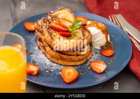 Pain grillé garni de fraises et de feuilles de menthe avec de la crème glacée arrosée de sauce caramel et de sucre en poudre sur une assiette bleue accompagnée de Banque D'Images