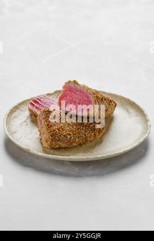 Sur une assiette simple, les tranches de thon enrobées de graines de sésame présentent une belle viande rose, mettant en valeur les compétences culinaires. Parfaitement préparé, ce plat invit Banque D'Images