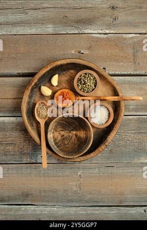 Une assiette en bois rustique présente un éventail d'épices, y compris du paprika, du sel et des herbes, aux côtés de gousses d'ail, disposées soigneusement sur un simple bois Banque D'Images