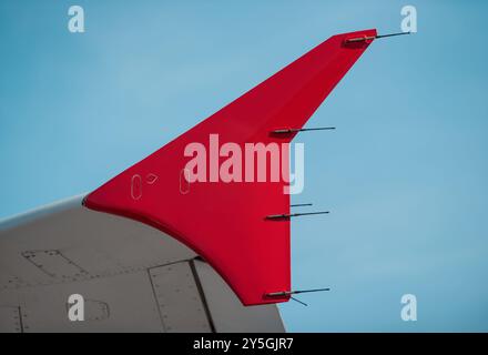 Pointe d'aile en forme de flèche rouge contre un ciel bleu clair par une journée ensoleillée. Gros plan sur les détails modernes de l'avion. Banque D'Images