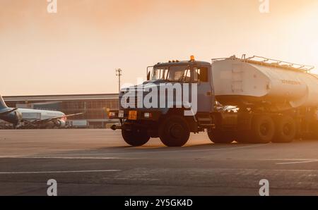 Camion de carburant d'aéroport au coucher du soleil. Ravitailleur d'aviation sur la plate-forme de camion KrAZ. Terminal de L'aéroport en arrière-plan. Banque D'Images