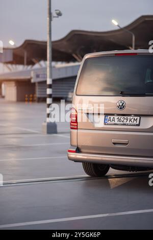 Beige VW transporter au dernier étage du garage de stationnement. Vue arrière de la fourgonnette Volkswagen T6 au crépuscule, terminal de l'aéroport en arrière-plan. Banque D'Images