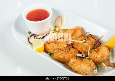 Délicieuses crevettes panées frites servies avec quartiers de citron vert et salade de légumes sur assiette blanche. Banque D'Images