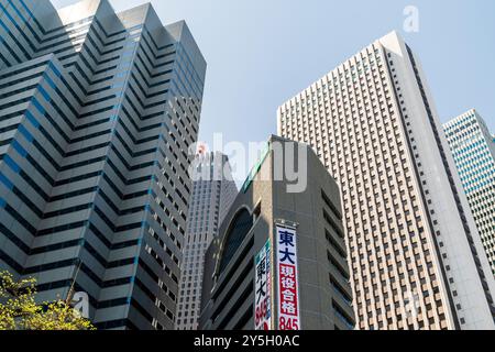 Vue sur la rue jusqu'au sommet de la tour Shinjuku l et le bâtiment du siège social SOMPO avec un fond de ciel bleu clair. Banque D'Images