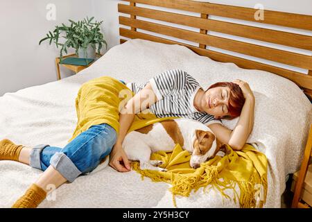 Femme dormant sur le lit avec son chien Jack Russell Terrier enveloppé dans un blanchet jaune. Banque D'Images