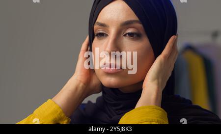 Grave irrité femme musulmane fille portant hijab dans le studio ajustant l'écharpe traditionnelle femme islamique fixant des vêtements mécontents modèle arabe soupir Banque D'Images