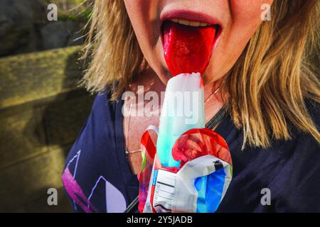 Gros plan d'une femme avec une langue tachée de rouge en mangeant du popsicle rouge, blanc et bleu. ÉTATS-UNIS. Banque D'Images