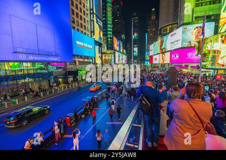 Vue nocturne animée de Times Square avec de grands panneaux d'affichage, des lumières vives et des gens debout sur les escaliers rouges à New York. ÉTATS-UNIS. Banque D'Images