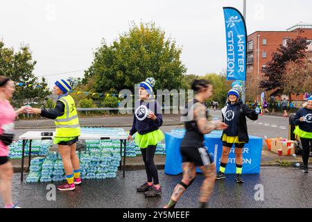 Dimanche 22 septembre 2024 - Warrington, Cheshire, Angleterre, Royaume-Uni - Un festival de course à pied sur des routes ouvertes et fermées a eu lieu. Les femmes se sont habillées et se sont amusées à distribuer de l'eau à une station d'eau. Les coureurs passent dans un flou. Crédit : John Hopkins/Alamy Live News Banque D'Images